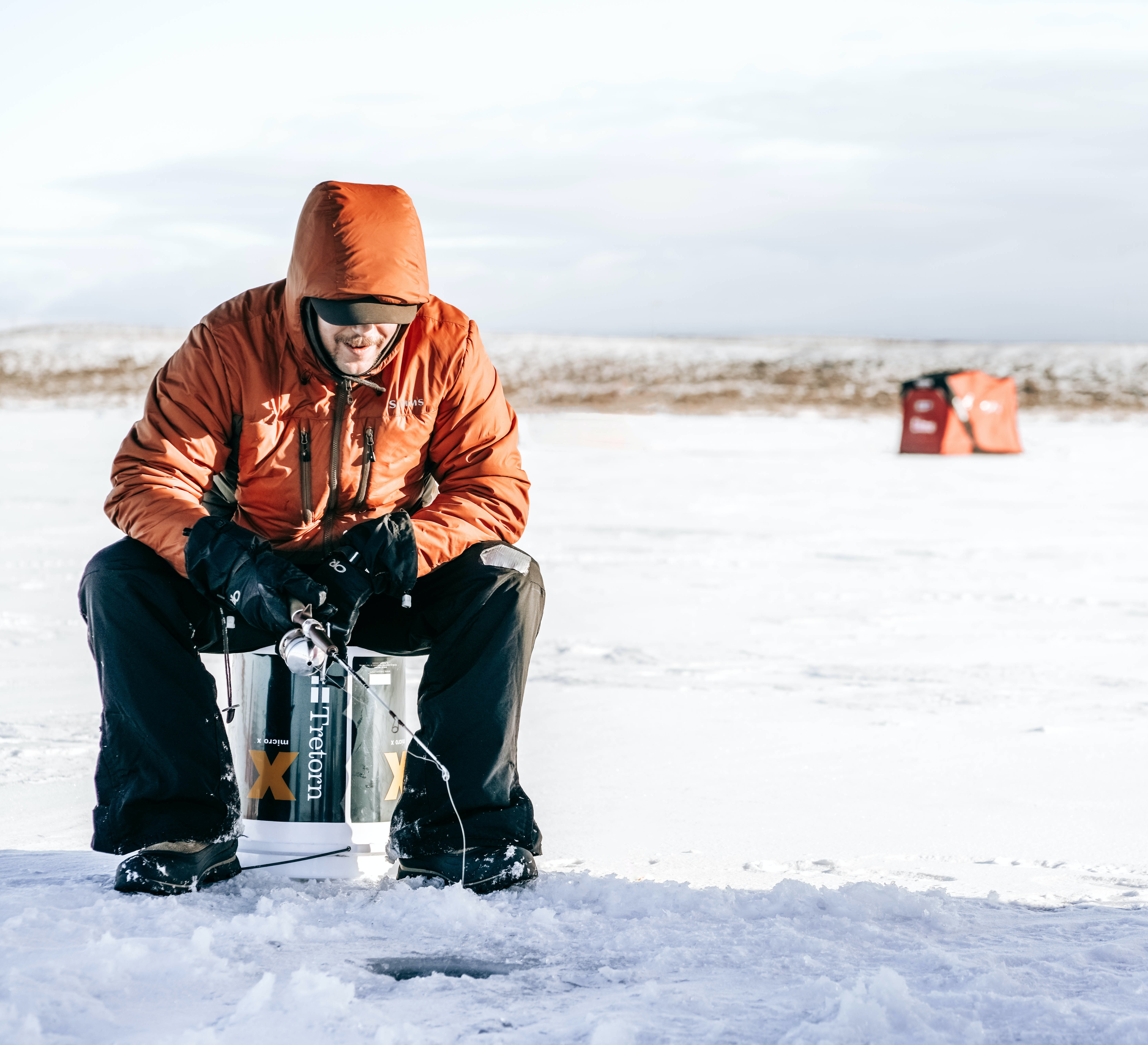 Ice fisherman sitting in the snow with an orange jacket